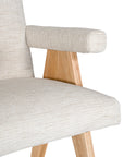 Modern oak dining chair with upholstered seat and backrest in a soft neutral fabric, featuring angled legs and cushioned armrests for comfort