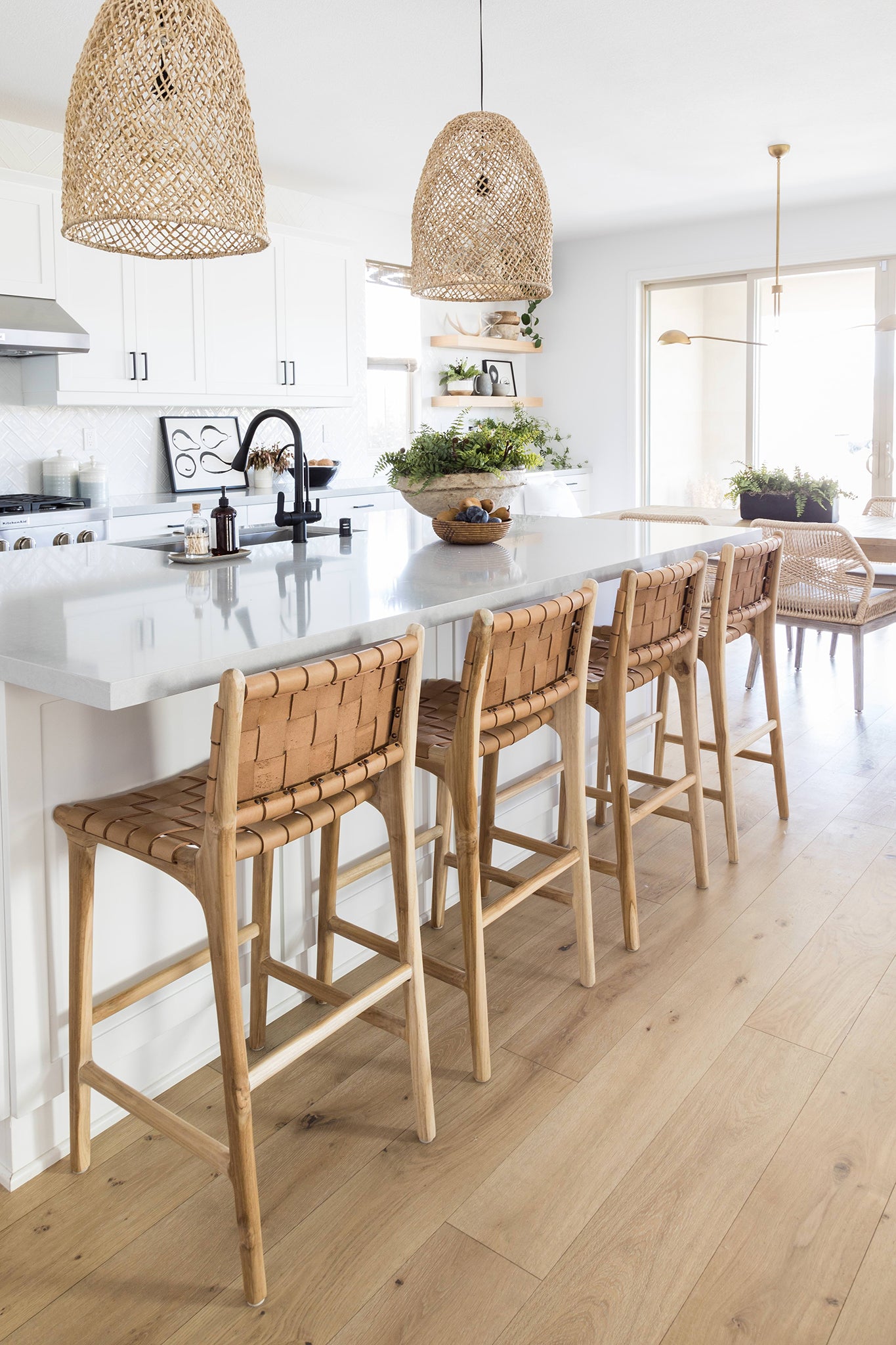 Bright and airy coastal kitchen featuring woven pendant lights, a marble island, and natural leather woven barstools for a relaxed, contemporary feel