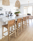 Bright and airy coastal kitchen featuring woven pendant lights, a marble island, and natural leather woven barstools for a relaxed, contemporary feel