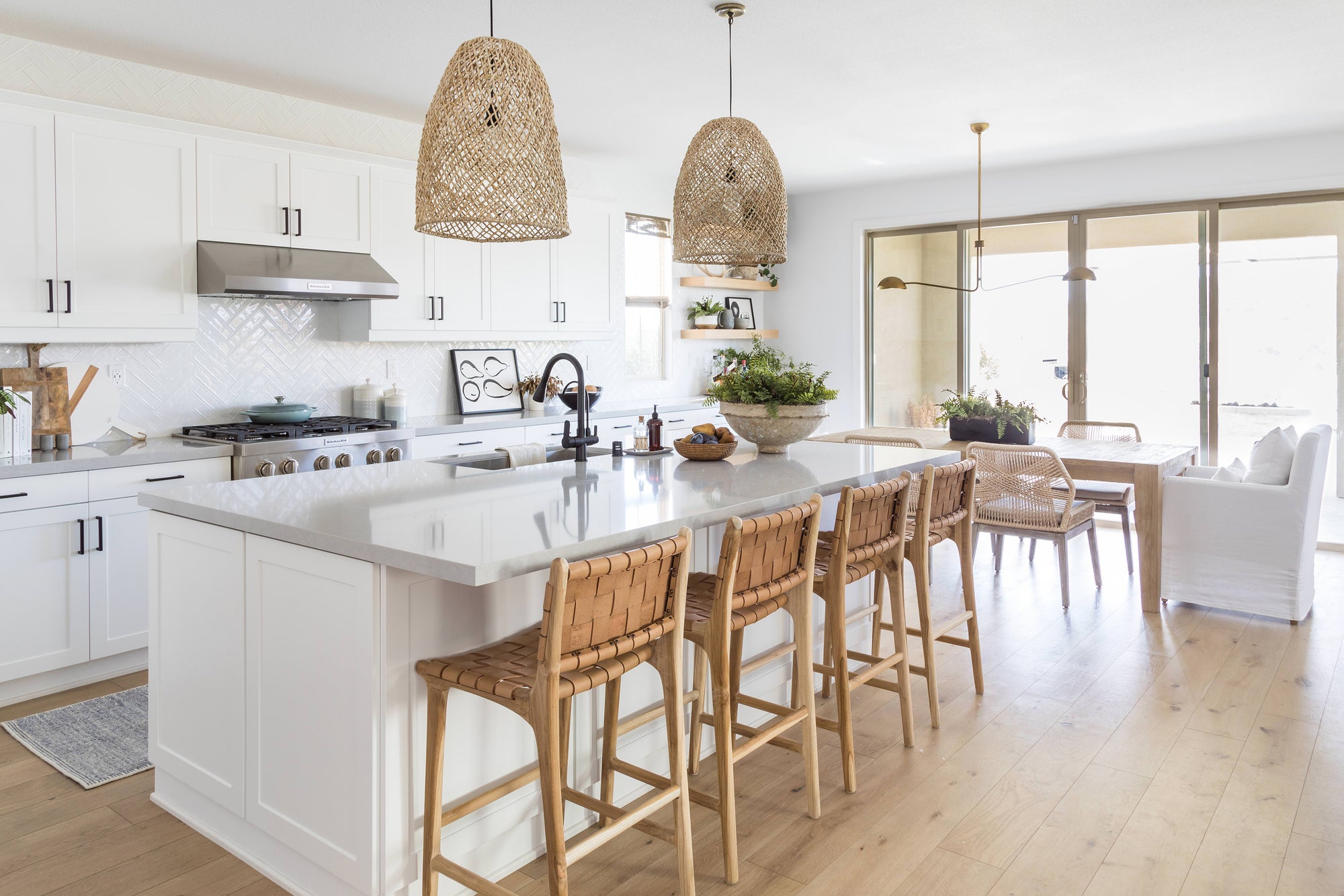 Bright and airy coastal kitchen featuring woven pendant lights, a marble island, and natural leather woven barstools for a relaxed, contemporary feel