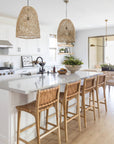 Bright and airy coastal kitchen featuring woven pendant lights, a marble island, and natural leather woven barstools for a relaxed, contemporary feel