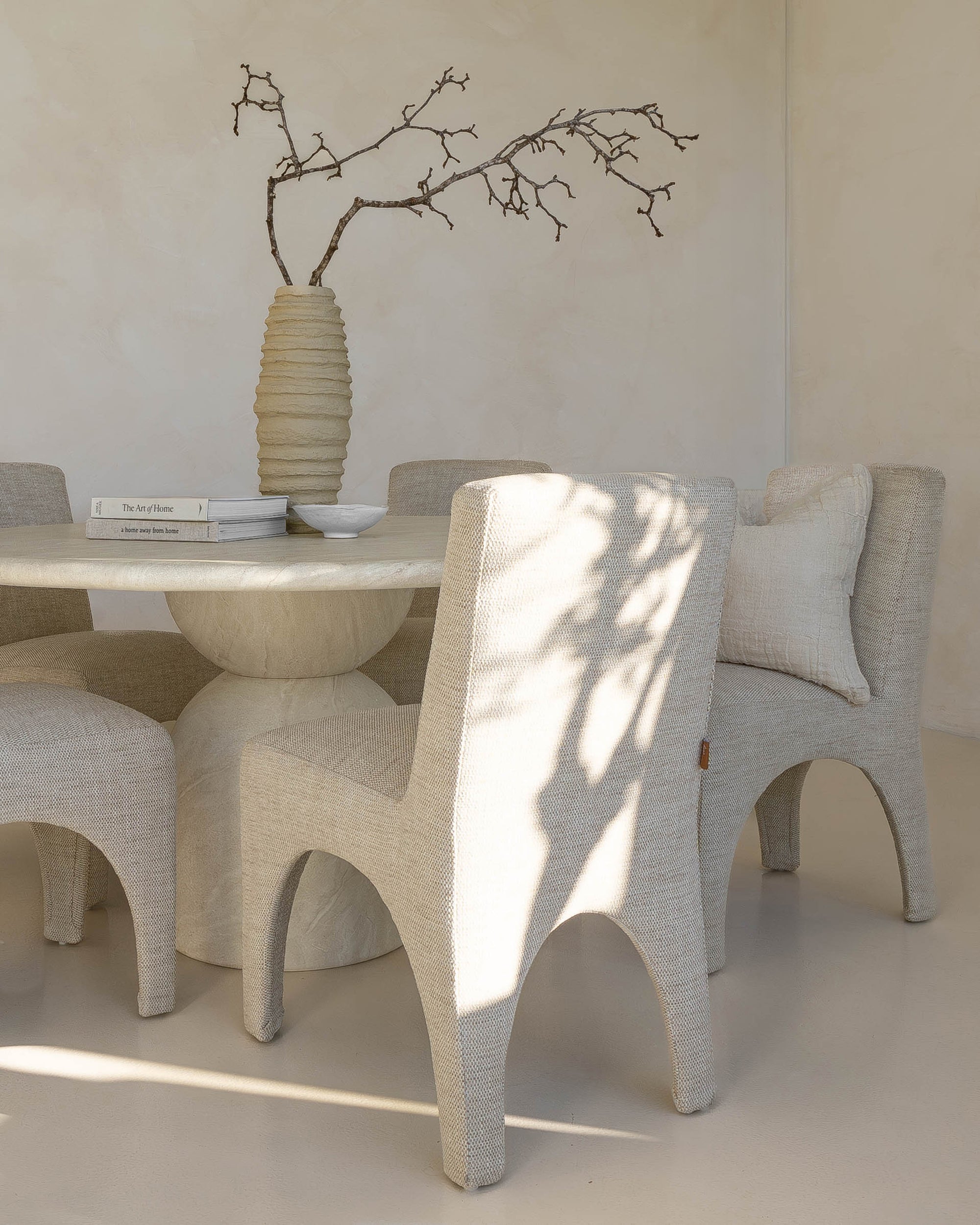 Modern dining room with a sculptural travertine table, textured upholstered chairs, and a handcrafted paper mâché vase, creating a serene and elegant space