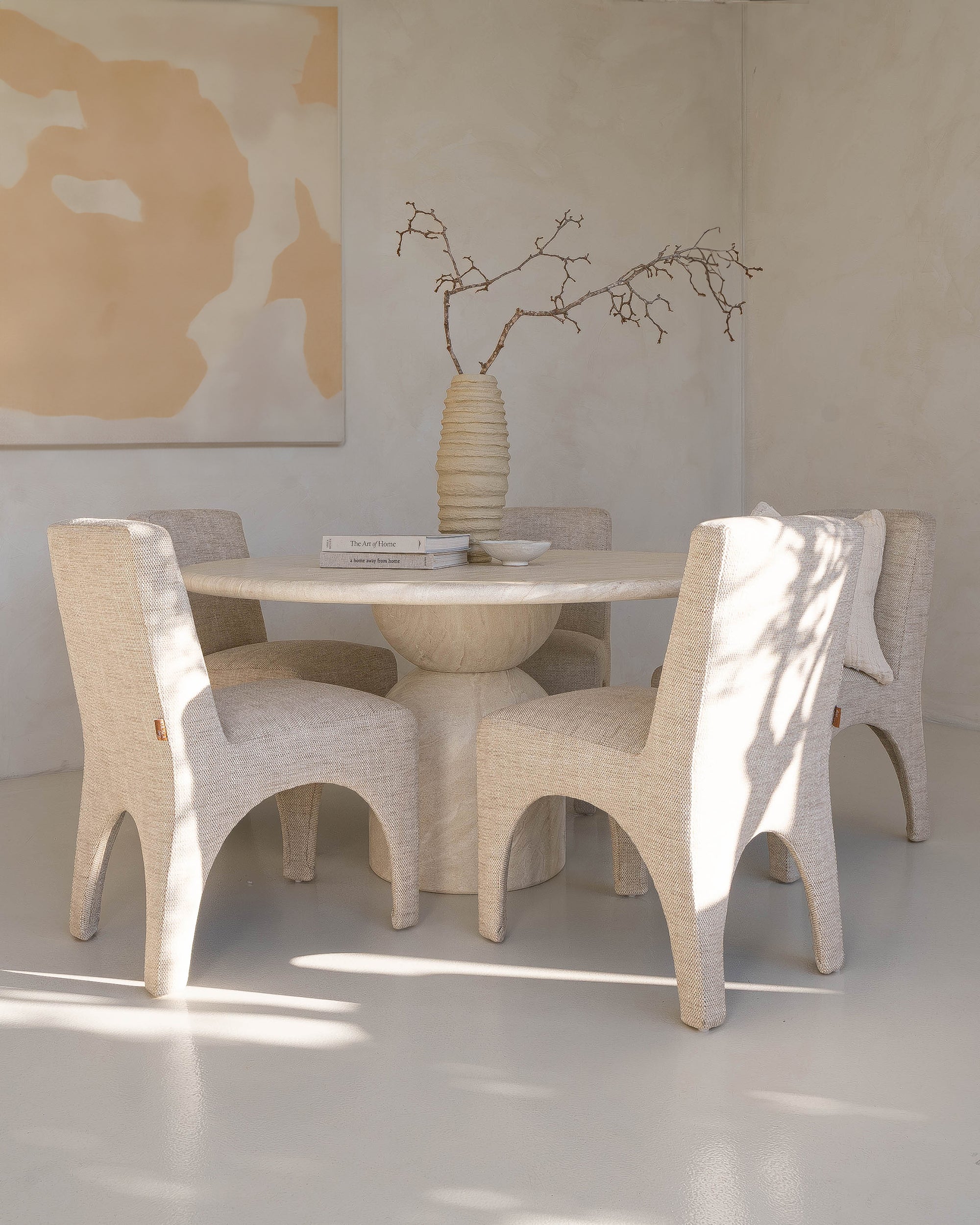 Modern dining room with a sculptural travertine table, textured upholstered chairs, and a handcrafted paper mâché vase, creating a serene and elegant space