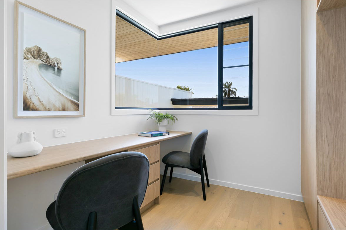 Minimalist home office featuring a sleek wooden desk and two black chairs with timber legs, complemented by natural light and neutral decor