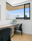 Minimalist home office featuring a sleek wooden desk and two black chairs with timber legs, complemented by natural light and neutral decor