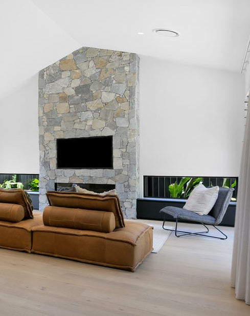 KULALA Living modern living room featuring a striking stone fireplace, tan leather sofa with bolster cushions, and a stylish black lounge chair with a metal frame, creating a warm and contemporary space