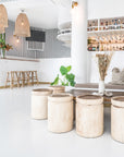 Coastal-inspired bar setting featuring handcrafted natural timber stools, woven pendant lights, and a relaxed seating area with earthy textures and neutral tones