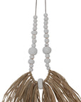 Decorative raffia and shell necklace on a black stand, featuring white wooden beads and natural raffia fringe, ideal for coastal and bohemian interiors