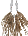 Decorative raffia and shell necklace on a black stand, featuring white wooden beads and natural raffia fringe, ideal for coastal and bohemian interiors