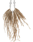 Decorative raffia and shell necklace on a black stand, featuring white wooden beads and natural raffia fringe, ideal for coastal and bohemian interiors