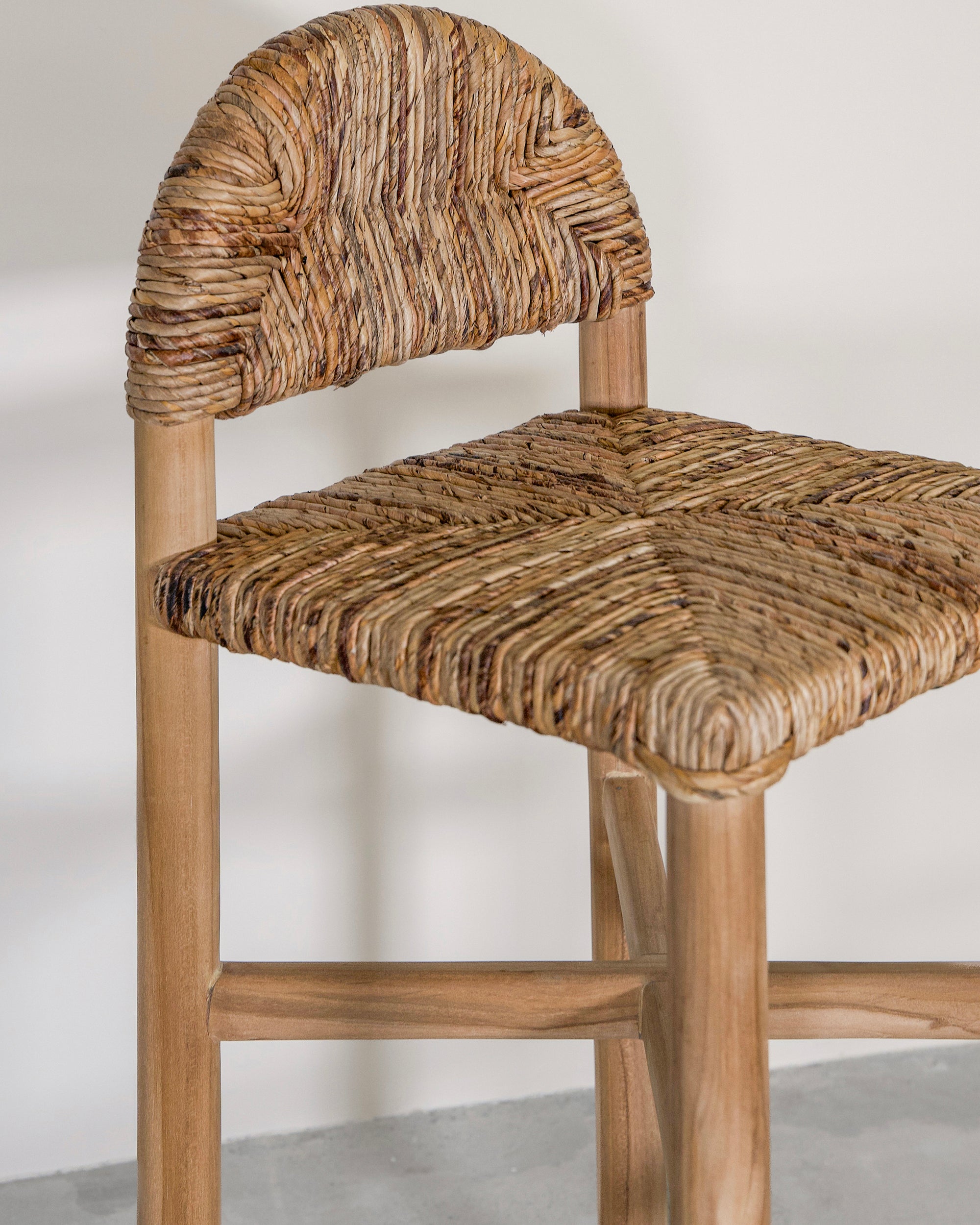 Handwoven rattan bar stool with a sturdy teak frame and curved backrest, showcasing organic texture and artisanal craftsmanship