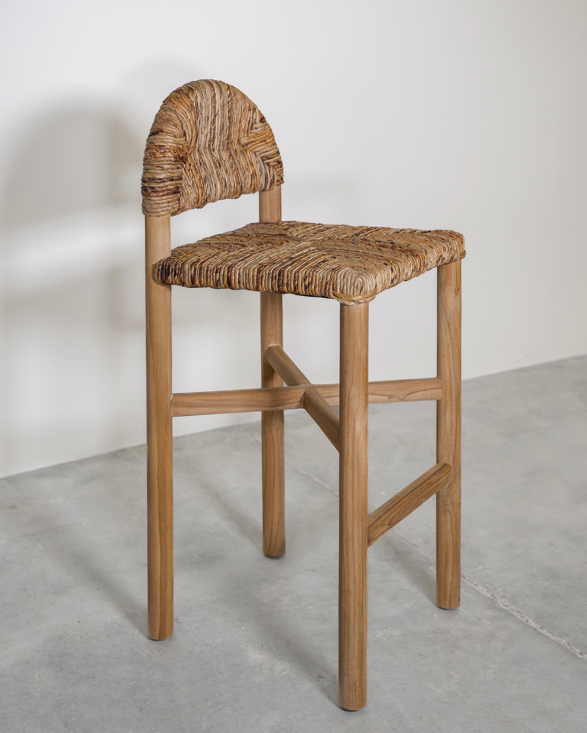 Handwoven rattan bar stool with a sturdy teak frame and curved backrest, showcasing organic texture and artisanal craftsmanship