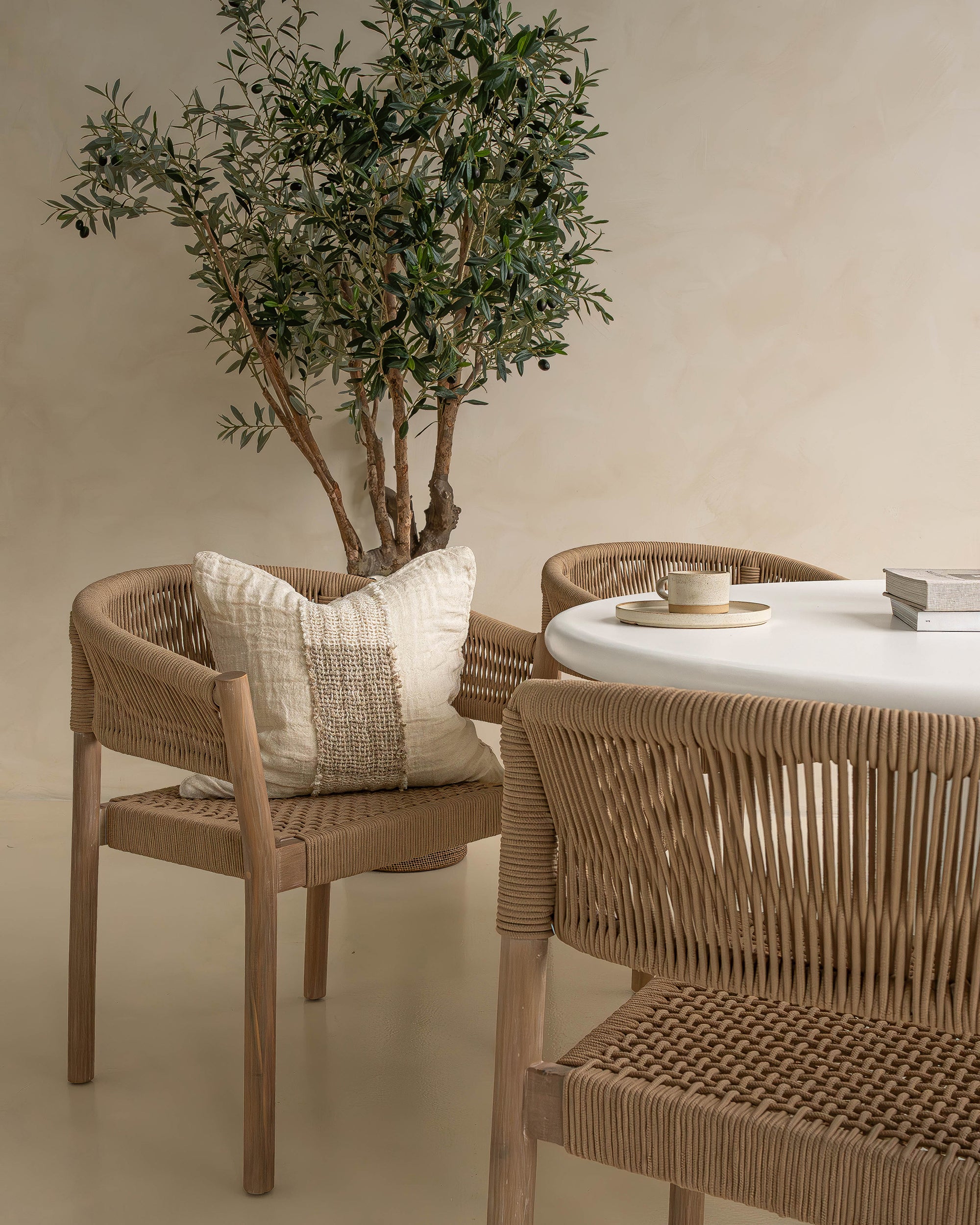 Elegant dining setup featuring natural rope dining chairs with teak frames paired with a round white table, creating a warm and inviting setting