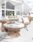 Luxurious outdoor lounge setting featuring woven rope chairs with white metal frames and matching round tables, styled with neutral cushions and coastal decor in a poolside alfresco space