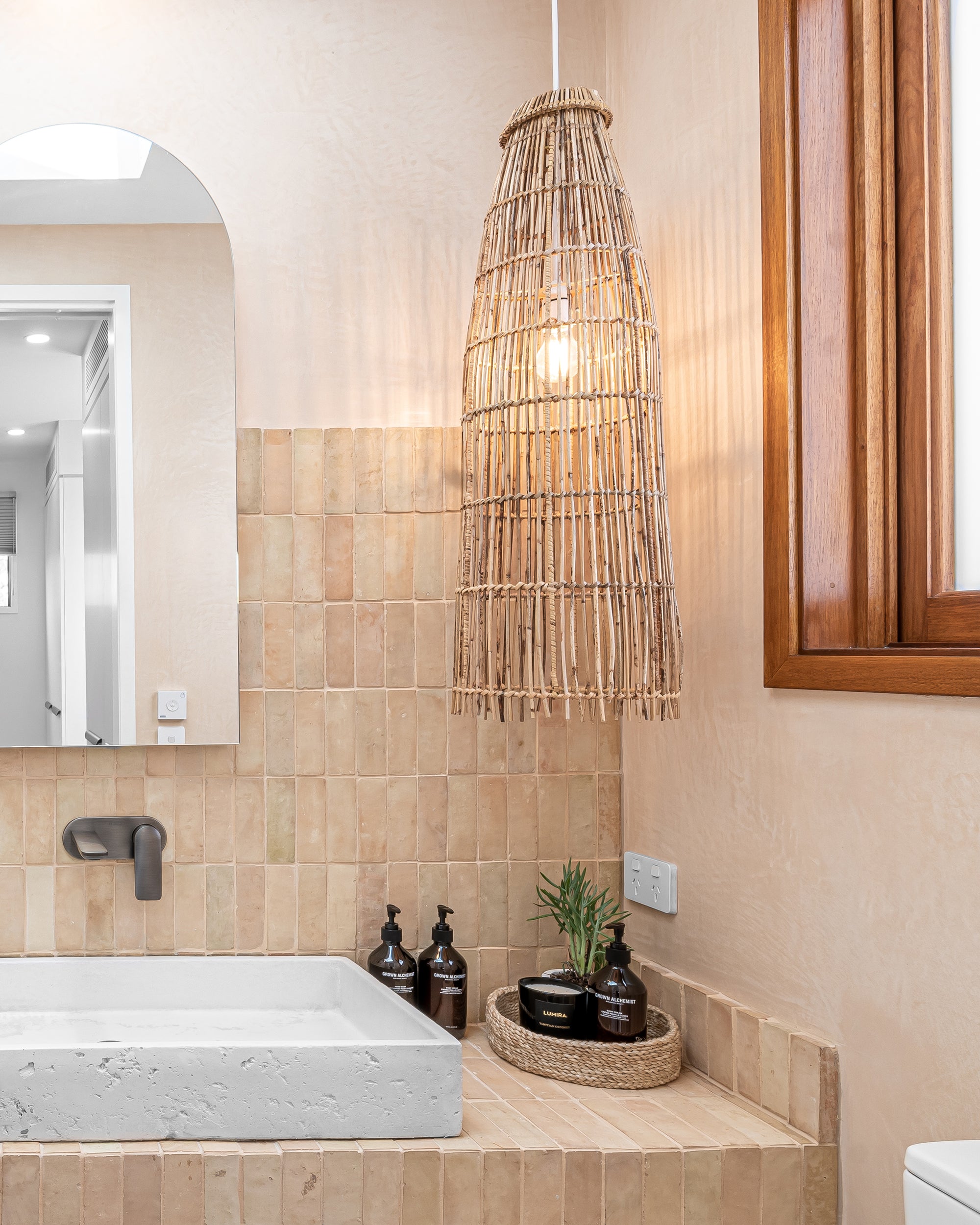 Bathroom featuring a natural rattan pendant light, a stone basin, and neutral-toned tiles, creating a warm and organic aesthetic