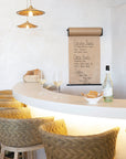 Coastal-inspired bar setting featuring woven rattan bar stools, a curved white counter, pendant lighting, and a handwritten menu on kraft paper, creating a relaxed dining ambiance