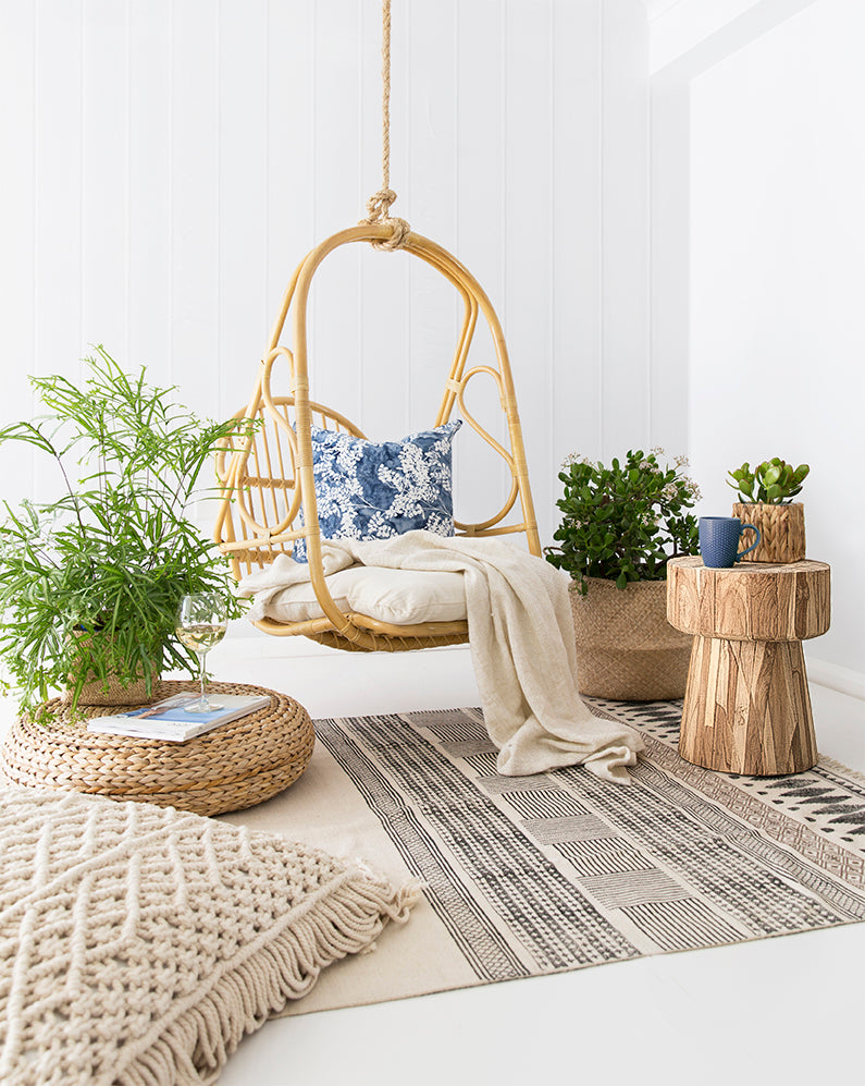 Bohemian-inspired space featuring a natural rattan hanging chair with plush cushions, a teak side table, and woven textures for a cosy and relaxed setting