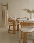 Coastal-inspired dining space featuring curved rattan dining chairs with upholstered seats, paired with a white fluted dining table. Styled with a ceramic vase, neutral-toned decor, and a wooden ladder with a draped throw for a relaxed, organic ambiance