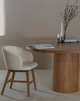 Elegant round oak pedestal dining table paired with a curved, upholstered dining chair in a soft neutral fabric, styled with minimalist decor