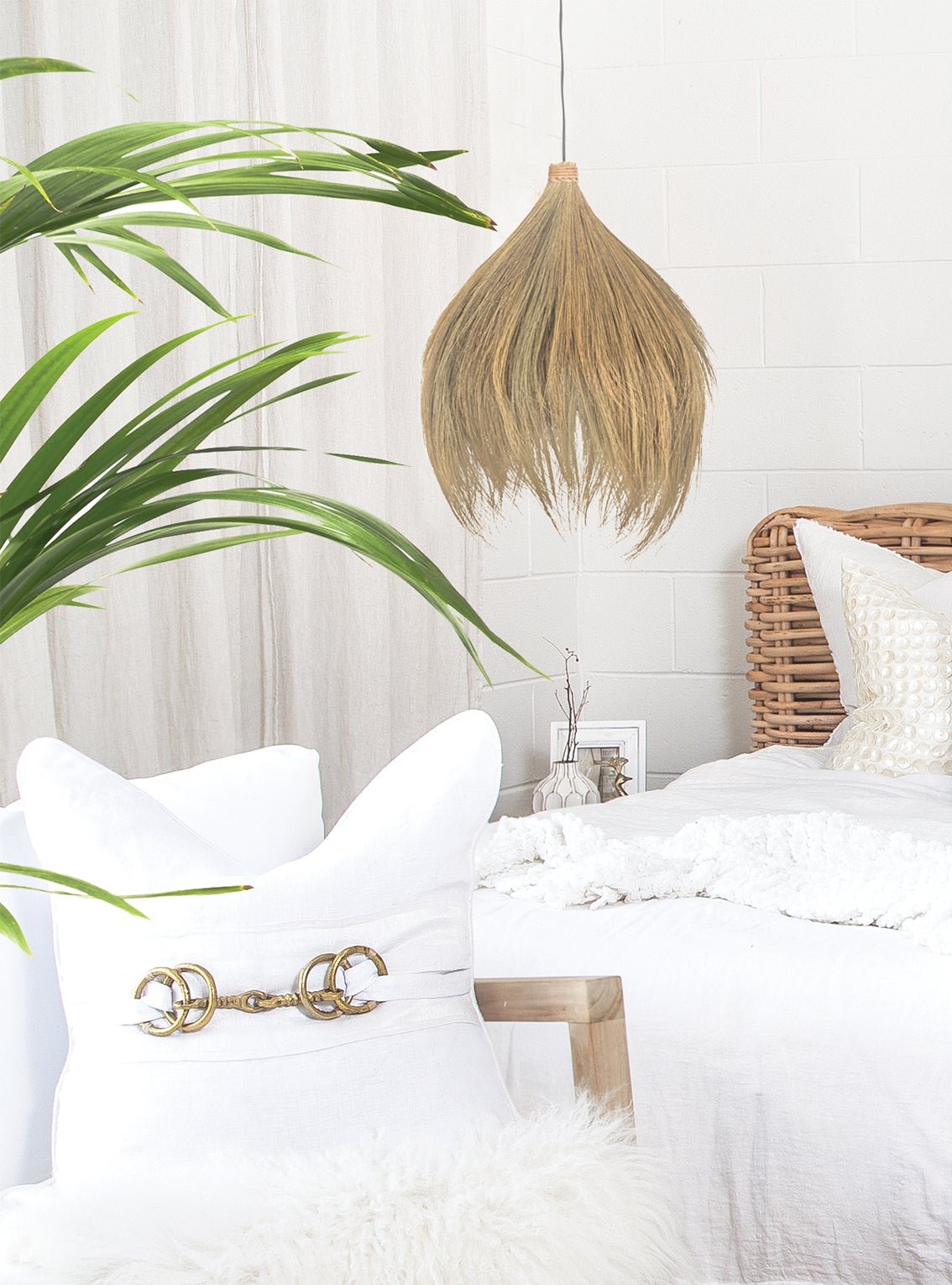 Coastal-inspired bedroom featuring a handwoven seagrass pendant light, rattan bed frame, and layered white linen styling