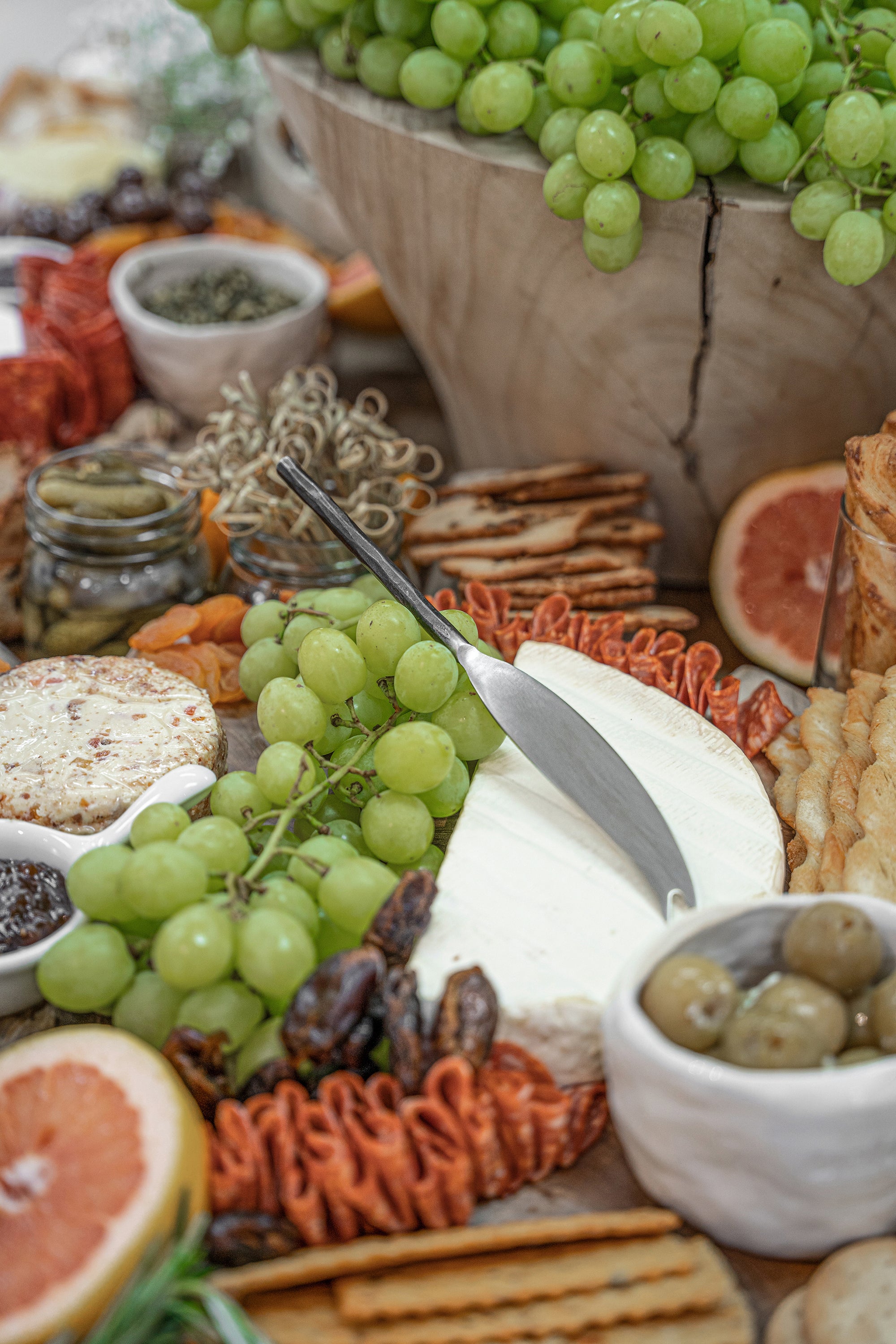 A beautifully styled grazing board featuring KULALA Living’s stainless steel cheese knife resting on a wheel of brie, surrounded by fresh green grapes, cured meats, crackers, and gourmet accompaniments. A refined and inviting spread for effortless entertaining