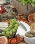 A beautifully styled grazing board featuring KULALA Living’s stainless steel cheese knife resting on a wheel of brie, surrounded by fresh green grapes, cured meats, crackers, and gourmet accompaniments. A refined and inviting spread for effortless entertaining