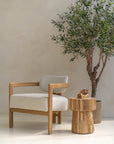 Minimalist interior featuring a teak armchair with boucle upholstery, paired with a natural teak side table and an olive tree for a serene, organic aesthetic