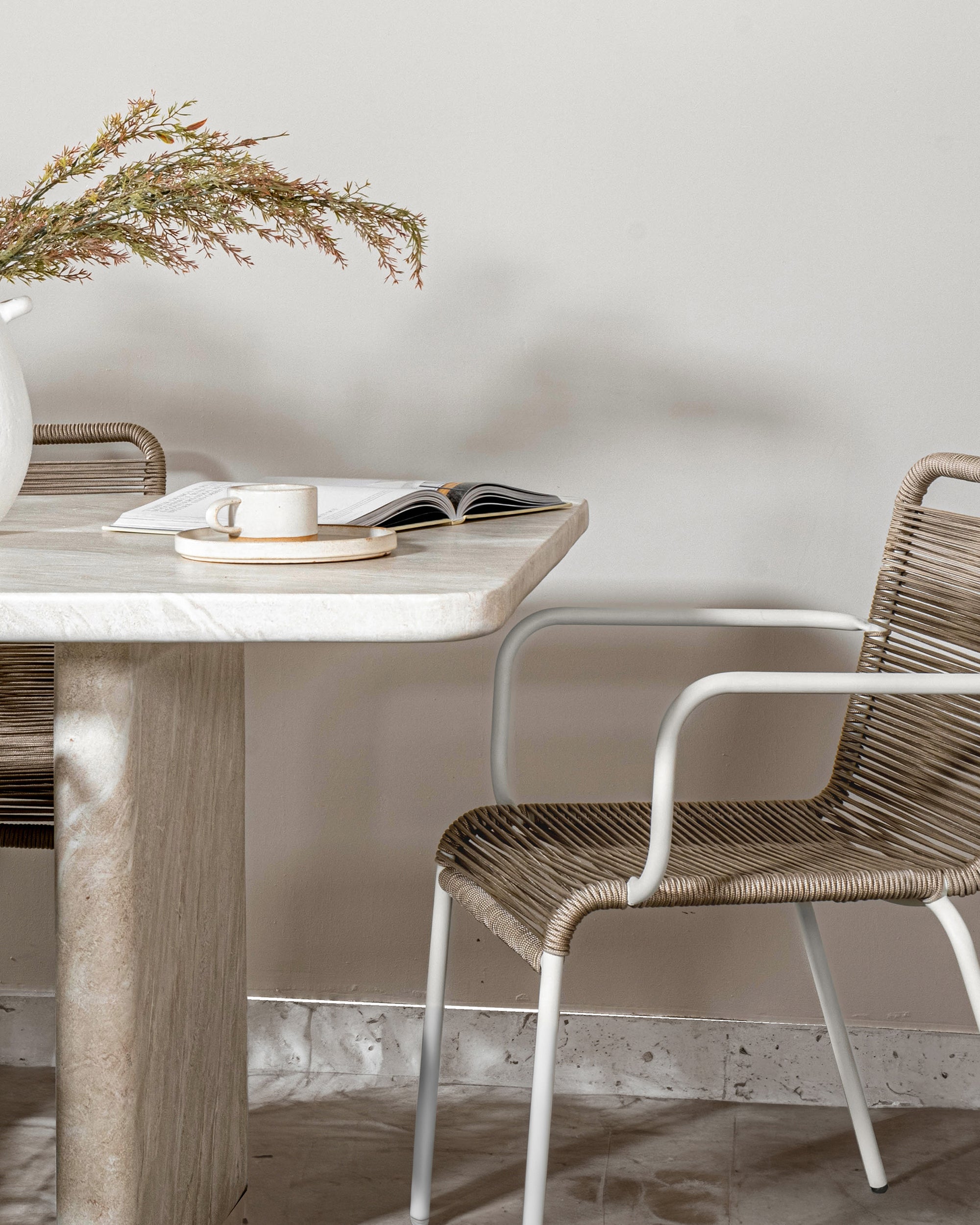 Outdoor dining chair with a white powder-coated metal frame and handwoven rope seat, styled with a natural stone dining table for an elegant alfresco setting