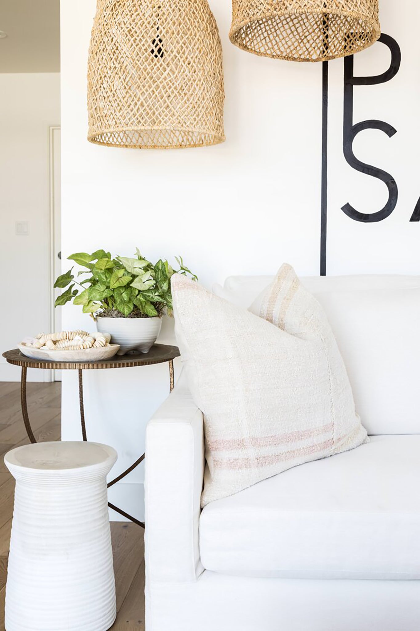 Relaxed coastal lounge featuring woven pendant lights, a white linen sofa, and soft neutral decor for a warm, inviting aesthetic