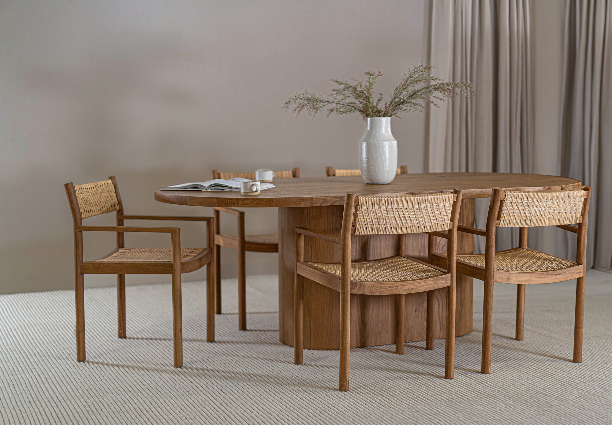 Elegant dining space featuring a solid oak dining table paired with teak and rattan dining chairs. A textured ceramic vase with greenery adds a natural touch to the setting