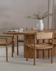 Elegant dining space featuring a solid oak dining table paired with teak and rattan dining chairs. A textured ceramic vase with greenery adds a natural touch to the setting