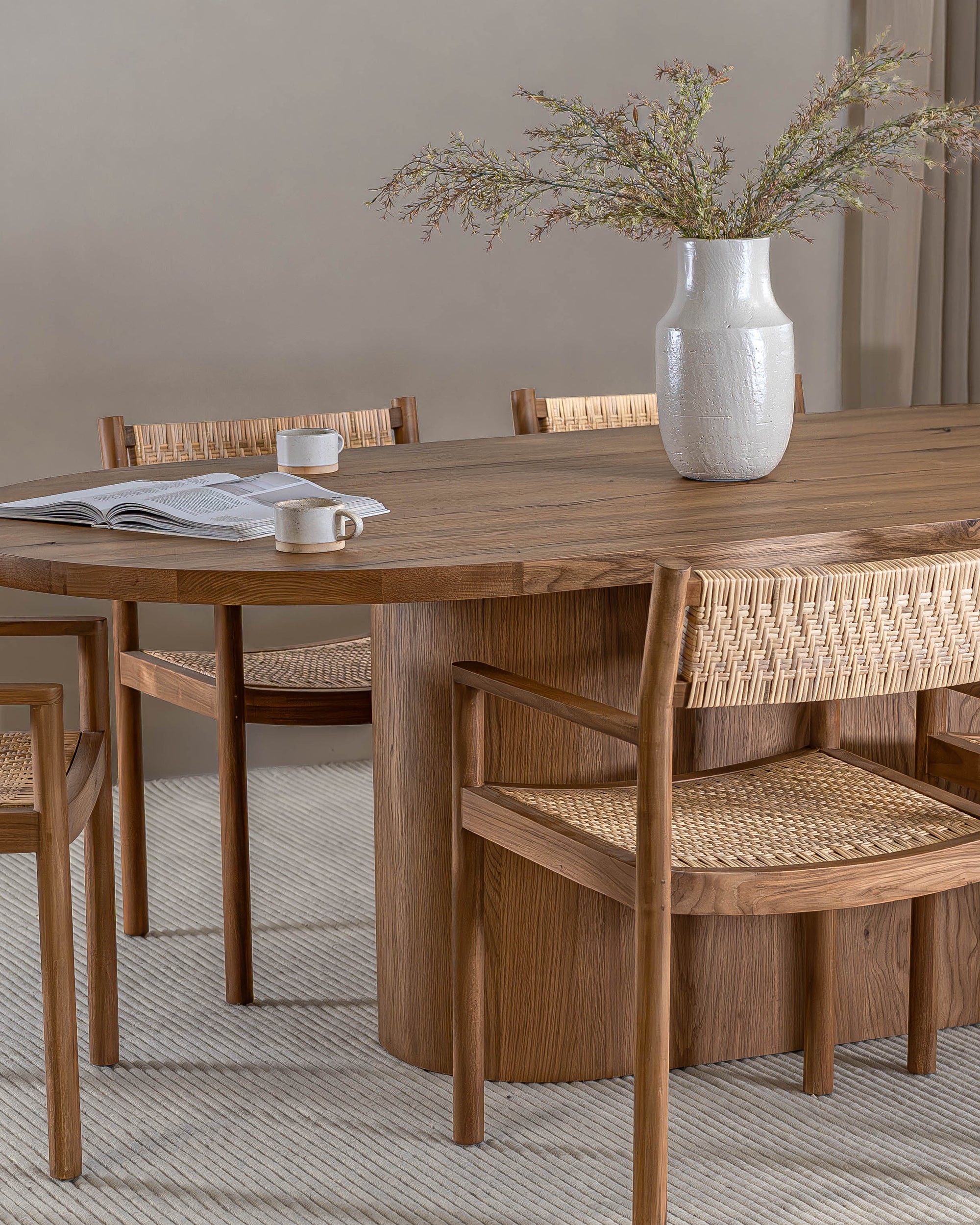 Elegant dining space featuring a solid oak dining table paired with teak and rattan dining chairs. A textured ceramic vase with greenery adds a natural touch to the setting