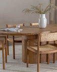 Elegant dining space featuring a solid oak dining table paired with teak and rattan dining chairs. A textured ceramic vase with greenery adds a natural touch to the setting